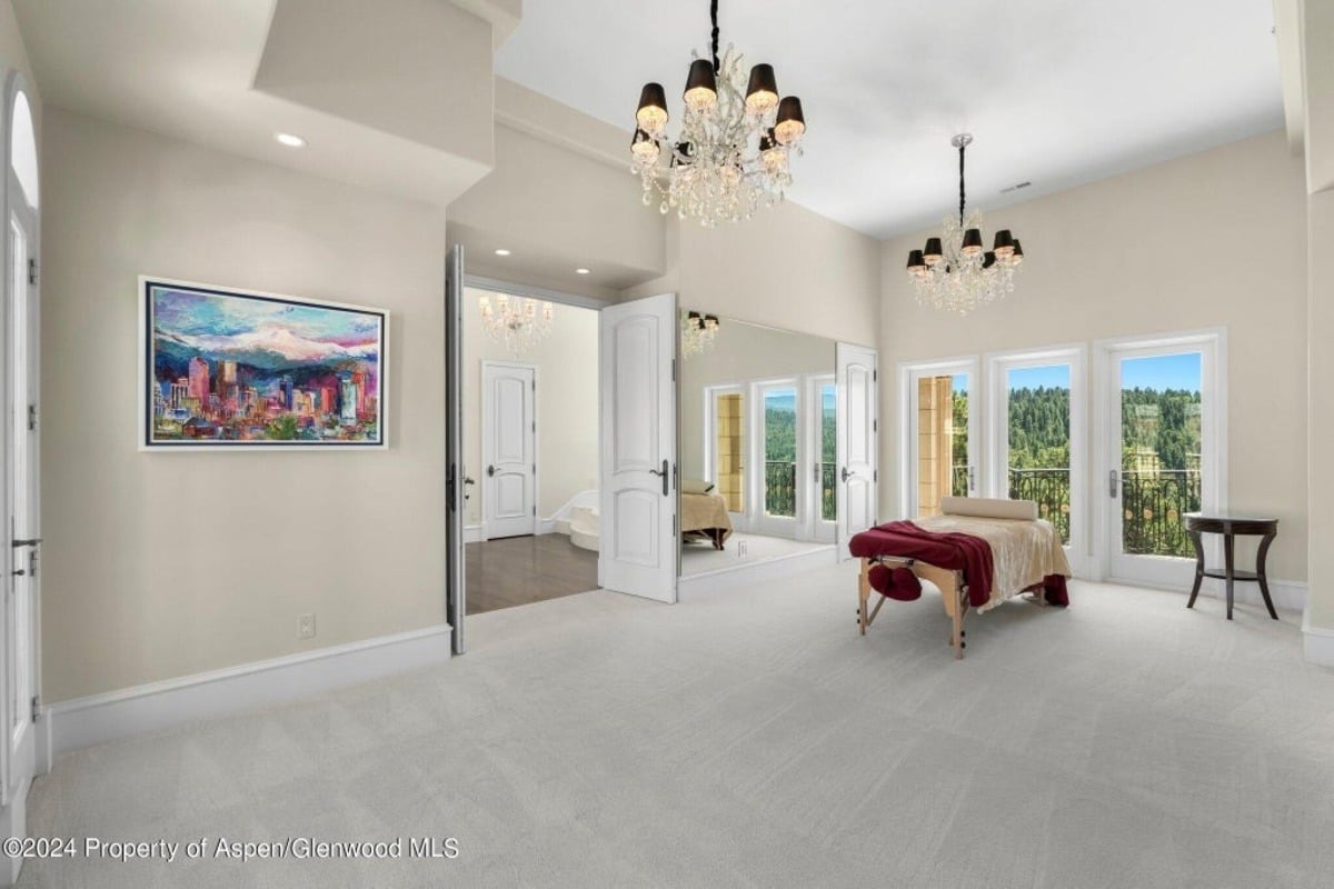 Wide, open space contains a massage table facing floor-to-ceiling windows and glass doors leading to a scenic balcony.