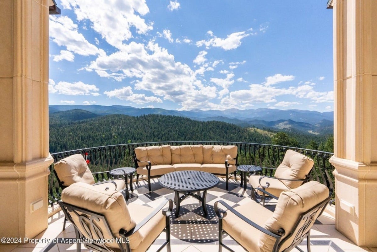 Plush beige cushions surround a round metal table, arranged on a balcony bordered by black iron railings.