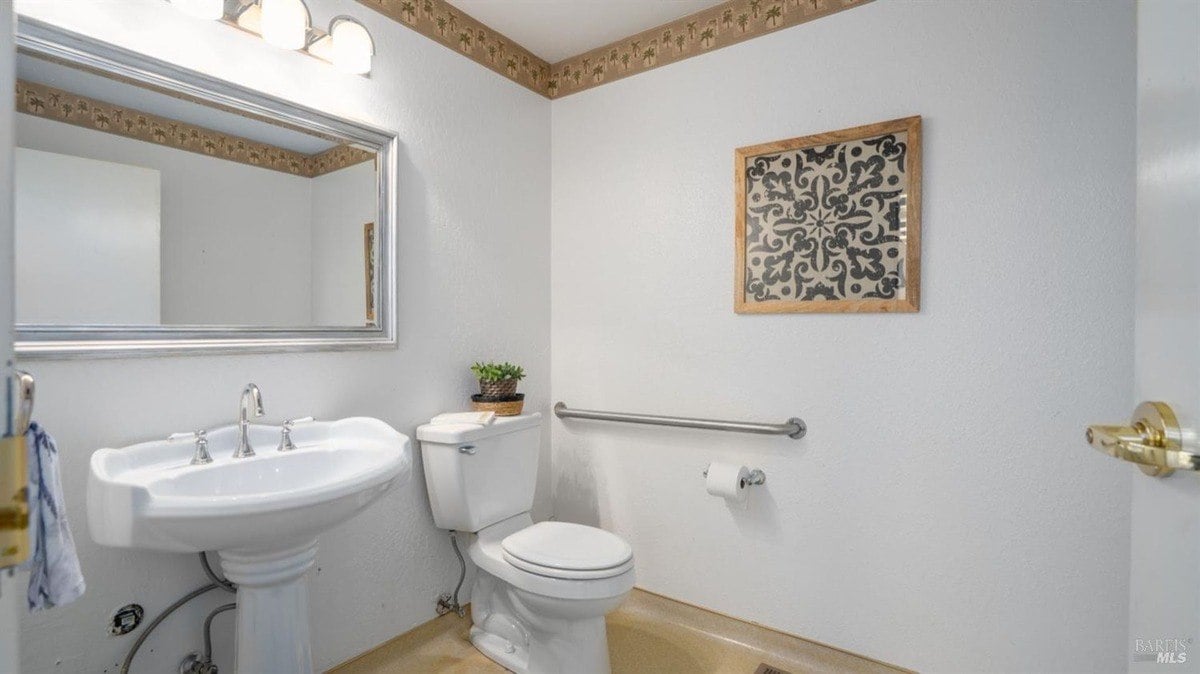Powder room features a pedestal sink, framed mirror, and tropical-patterned wallpaper border.