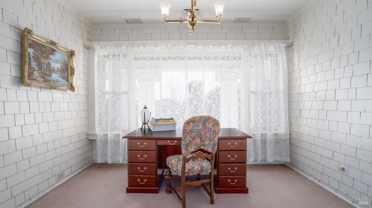 Sunroom showcases a desk, floral upholstered chair, lace curtains, and shingle-style wall panels.