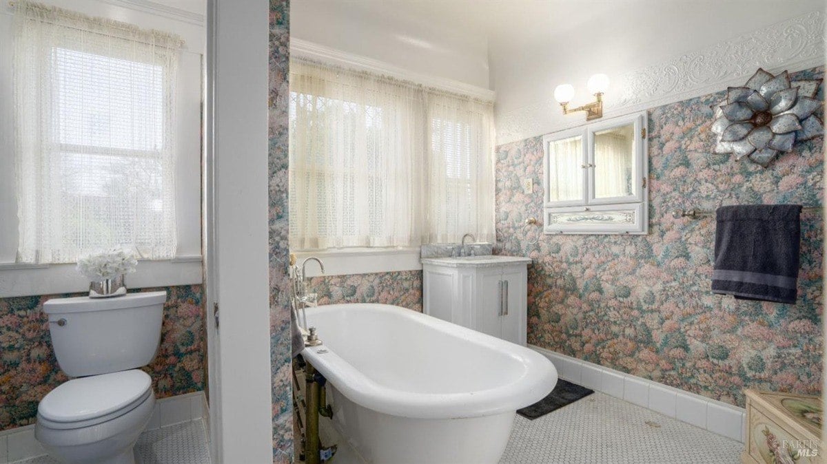 Bathroom displays a clawfoot tub, floral wallpaper, and bright windows with lace curtains.