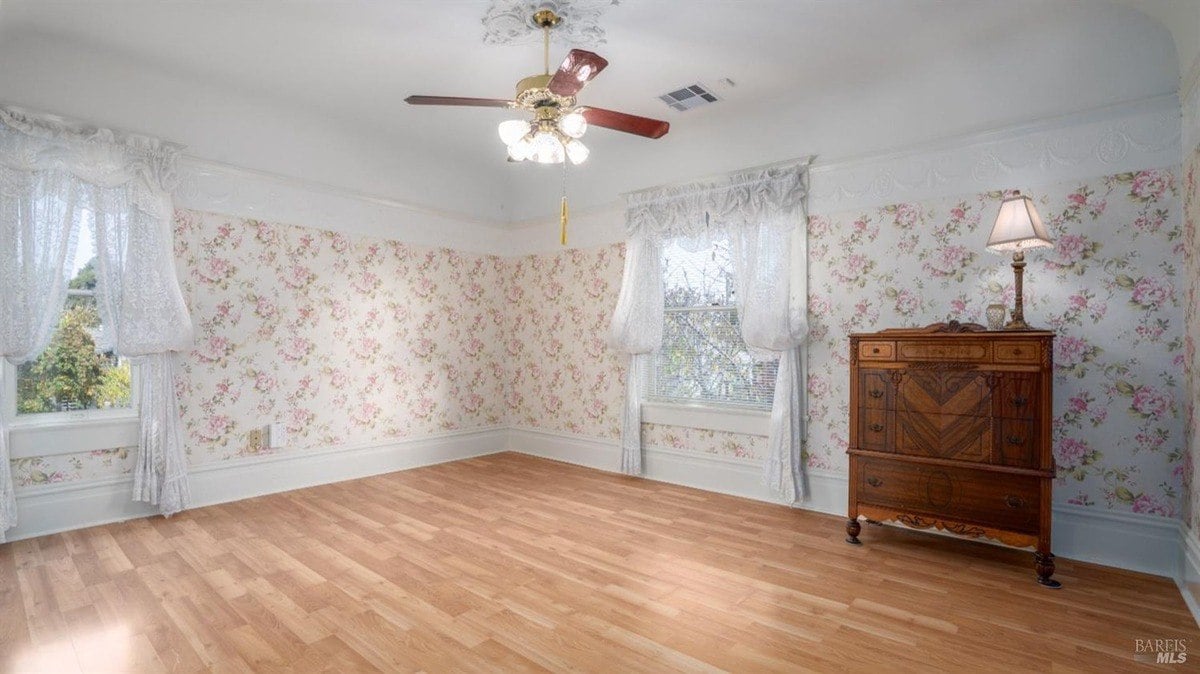 Room with wooden flooring, floral wallpaper, and a classic wooden dresser.
