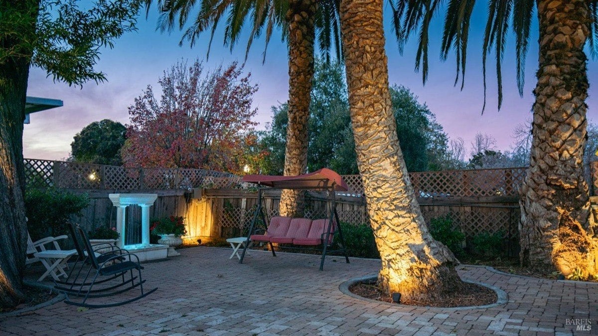 Tranquil patio space is lined with palm trees, brick flooring, and a relaxing swing seat.