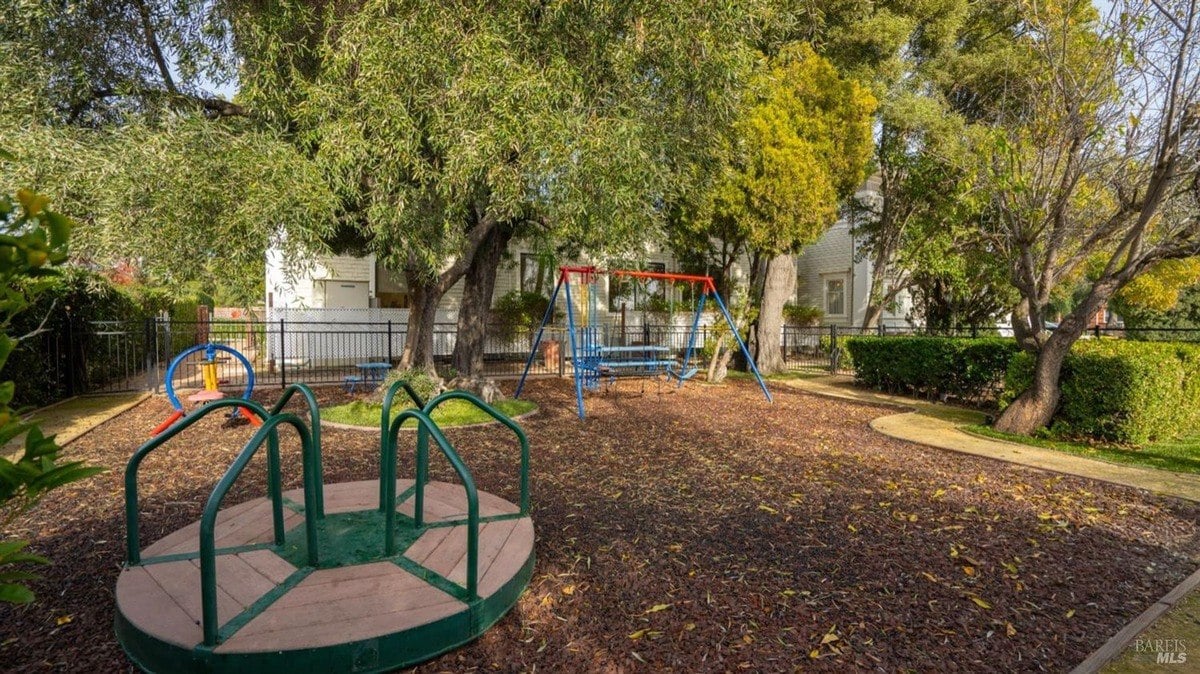 Playground area features a colorful merry-go-round, swing set, and mature trees providing shade.
