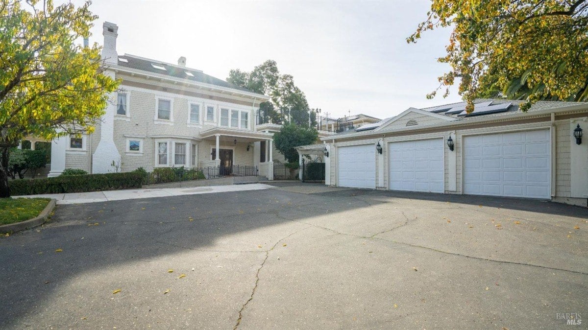 Driveway leads to an elegant house façade with a covered entrance and multiple garage doors.