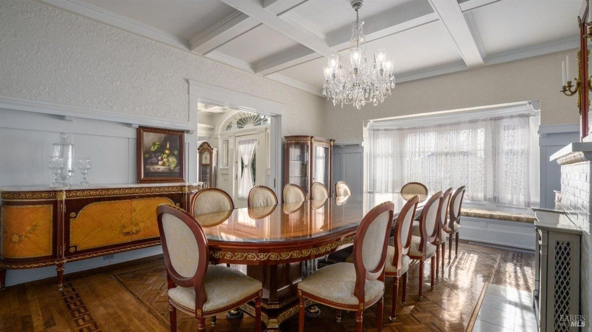 Formal dining room highlights a long polished table, chandelier, and built-in seating under a wide window with sheer drapes.