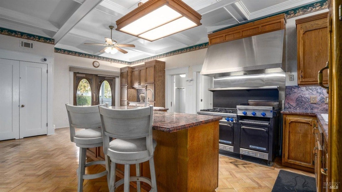 White kitchen with a large center island, double-door entry, and industrial-sized stove beneath a steel hood.
