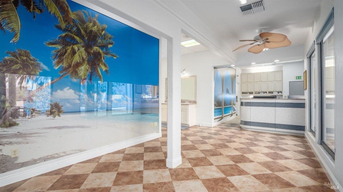 Reception area featuring tropical-themed murals, large windows, and a ceiling fan.