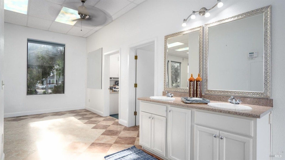 Dual-sink vanity in a brightly lit bathroom with a neutral color scheme and expansive mirrors.