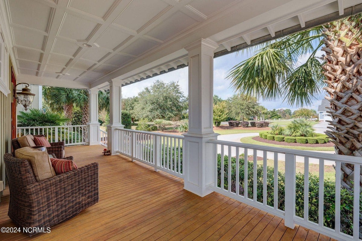 Porch has wood floor, white railing, and wicker furniture.