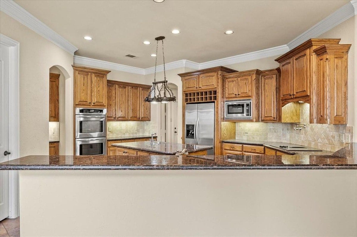 Front-facing kitchen area featuring wooden cabinetry, a granite countertop island, and stainless steel appliances.