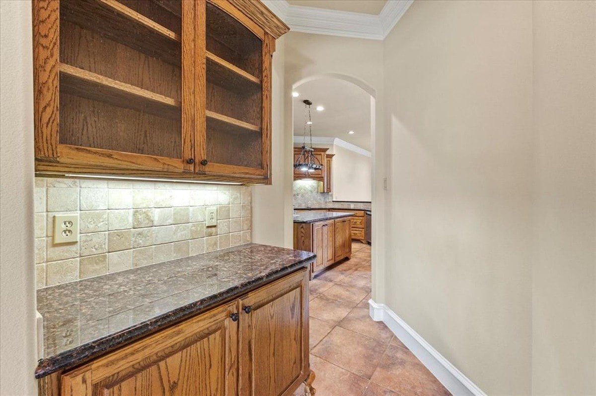 Butler's pantry with built-in shelves, granite counter, and tiled backsplash, leading to the main kitchen space.