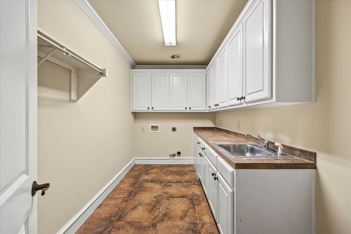 Laundry room equipped with upper and lower white cabinetry, countertop space, and a utility sink.