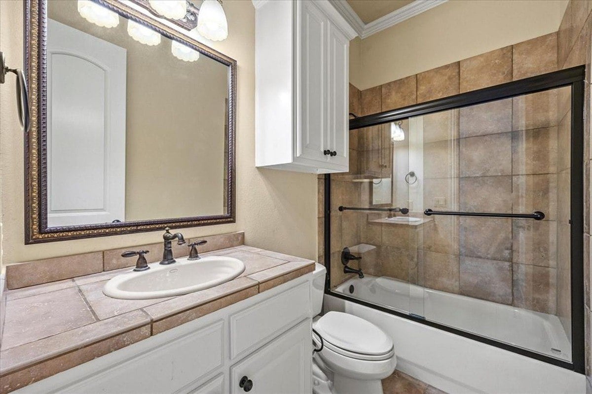 Bathroom with a framed mirror, tiled shower with glass enclosure, and white vanity topped with a stone countertop.