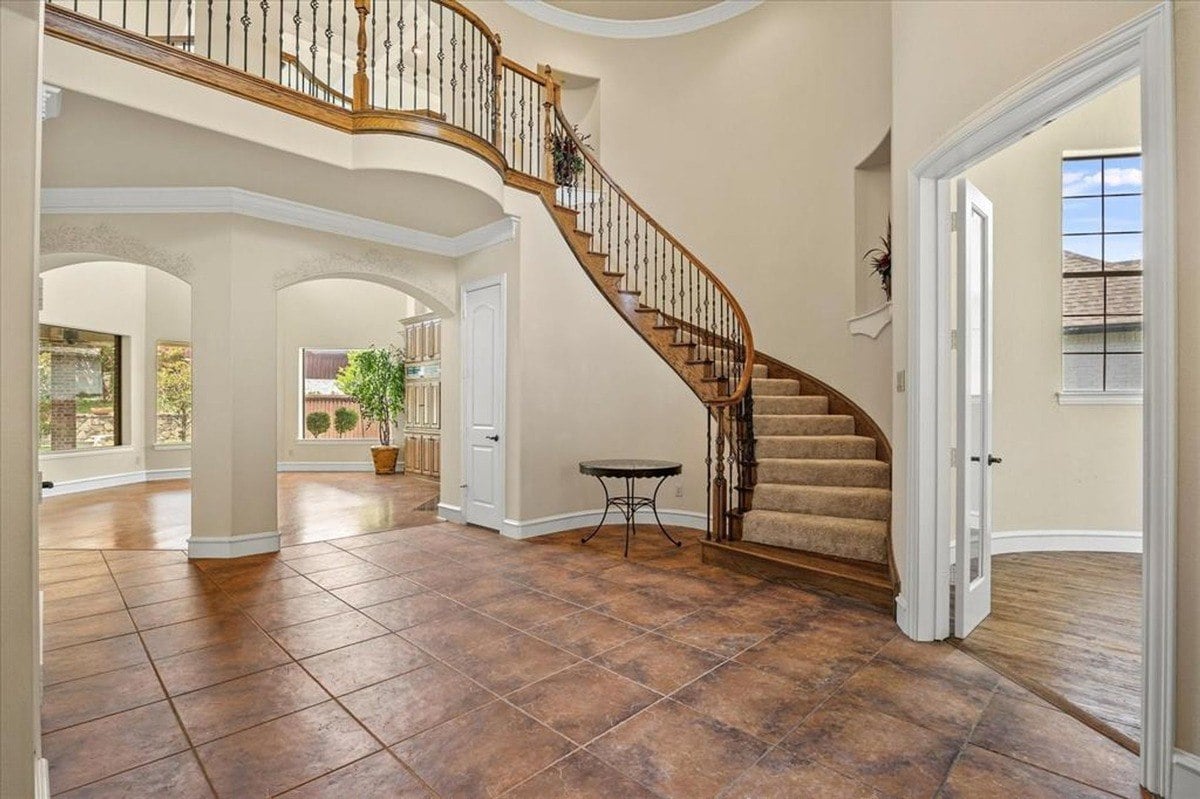 Grand staircase with wooden handrails and iron spindles sits in a high-ceilinged entryway.