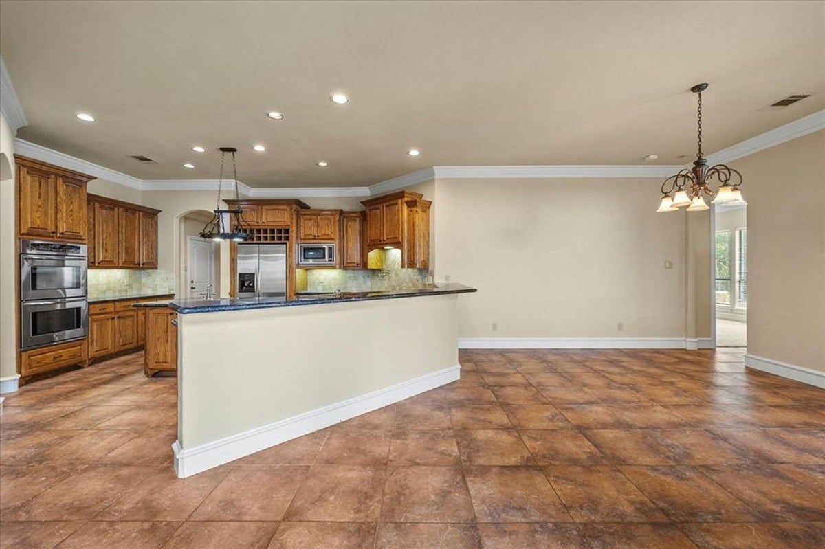 Kitchen with tiled floors, wooden cabinetry, granite countertops, and stainless steel appliances in a functional layout.