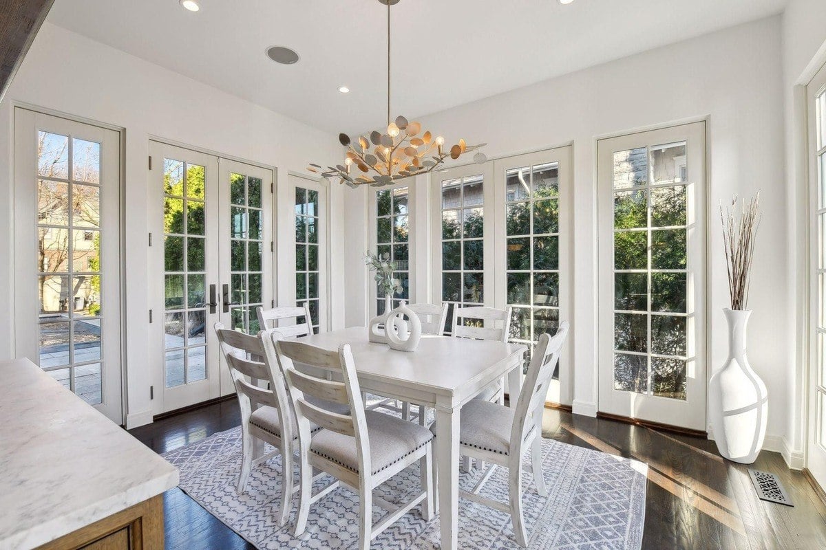 Dining room with white table and chairs, French doors, and a modern chandelier.