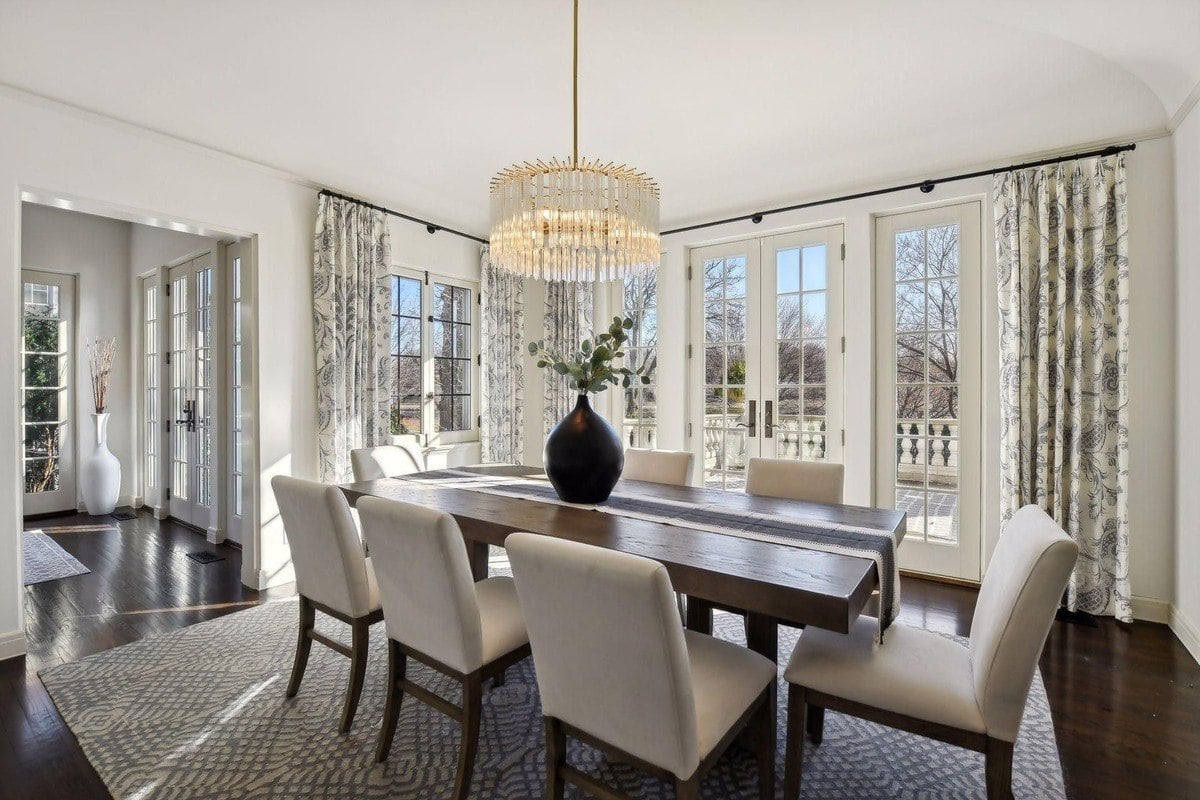 Dining room with a large wooden table, white chairs, and French doors leading to a balcony.