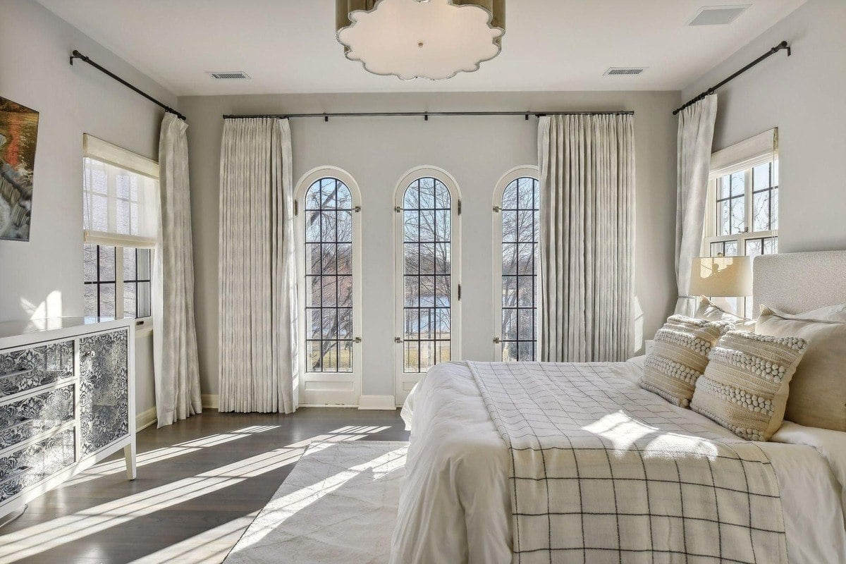 Bedroom with a bed, large windows, and light gray walls.