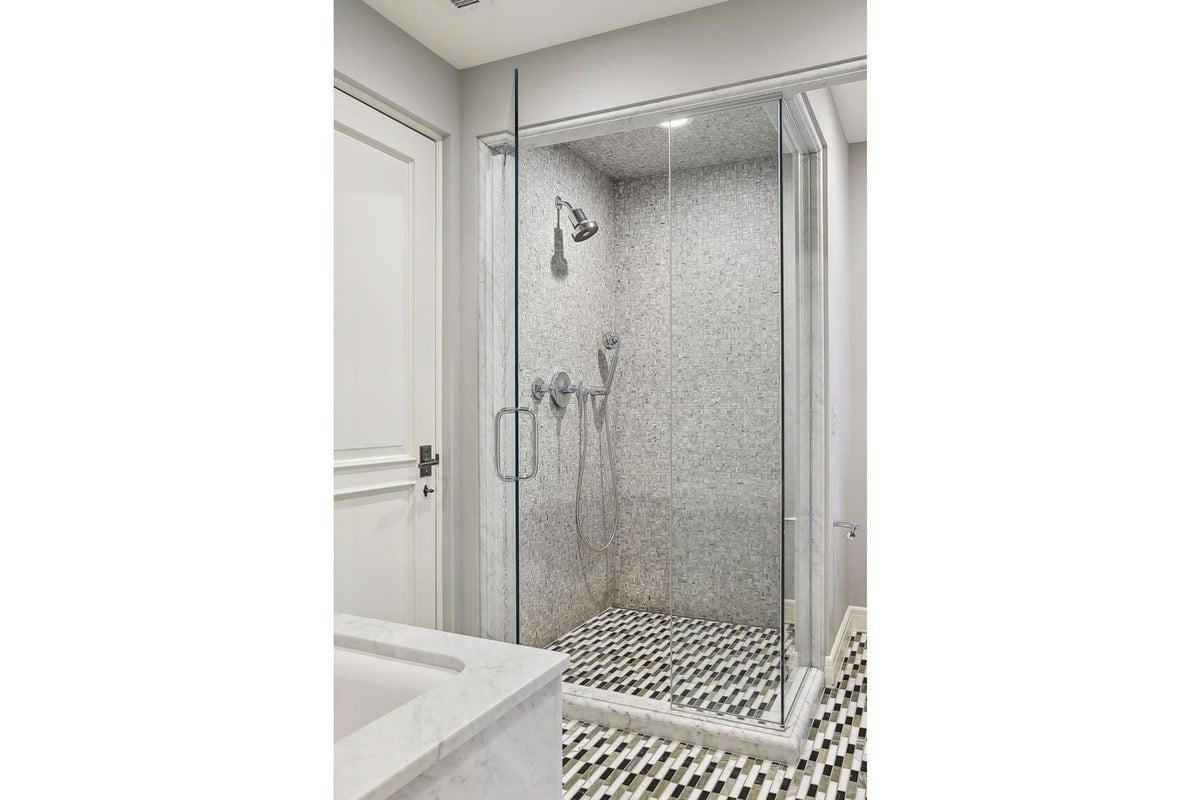 Shower with glass enclosure, marble tile, and gray walls.