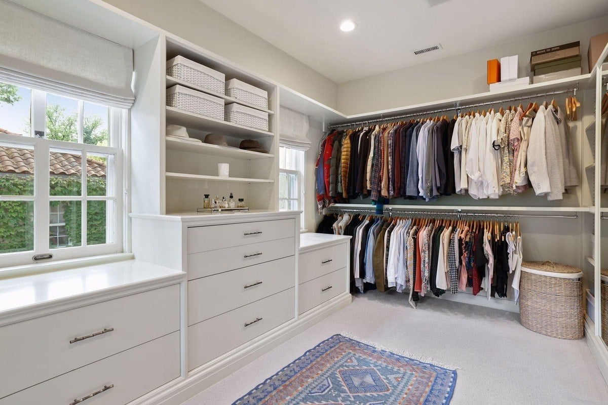 Walk-in closet with white built-in shelving and clothing hanging on racks.