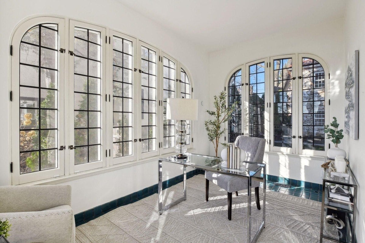 Home office with arched windows, glass desk, and light colored rug.