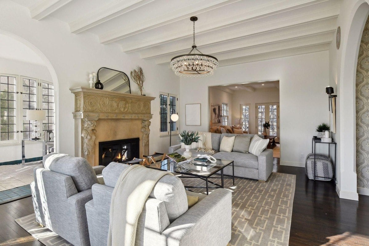 Living room with a large ornate fireplace, gray sofas, and a chandelier.