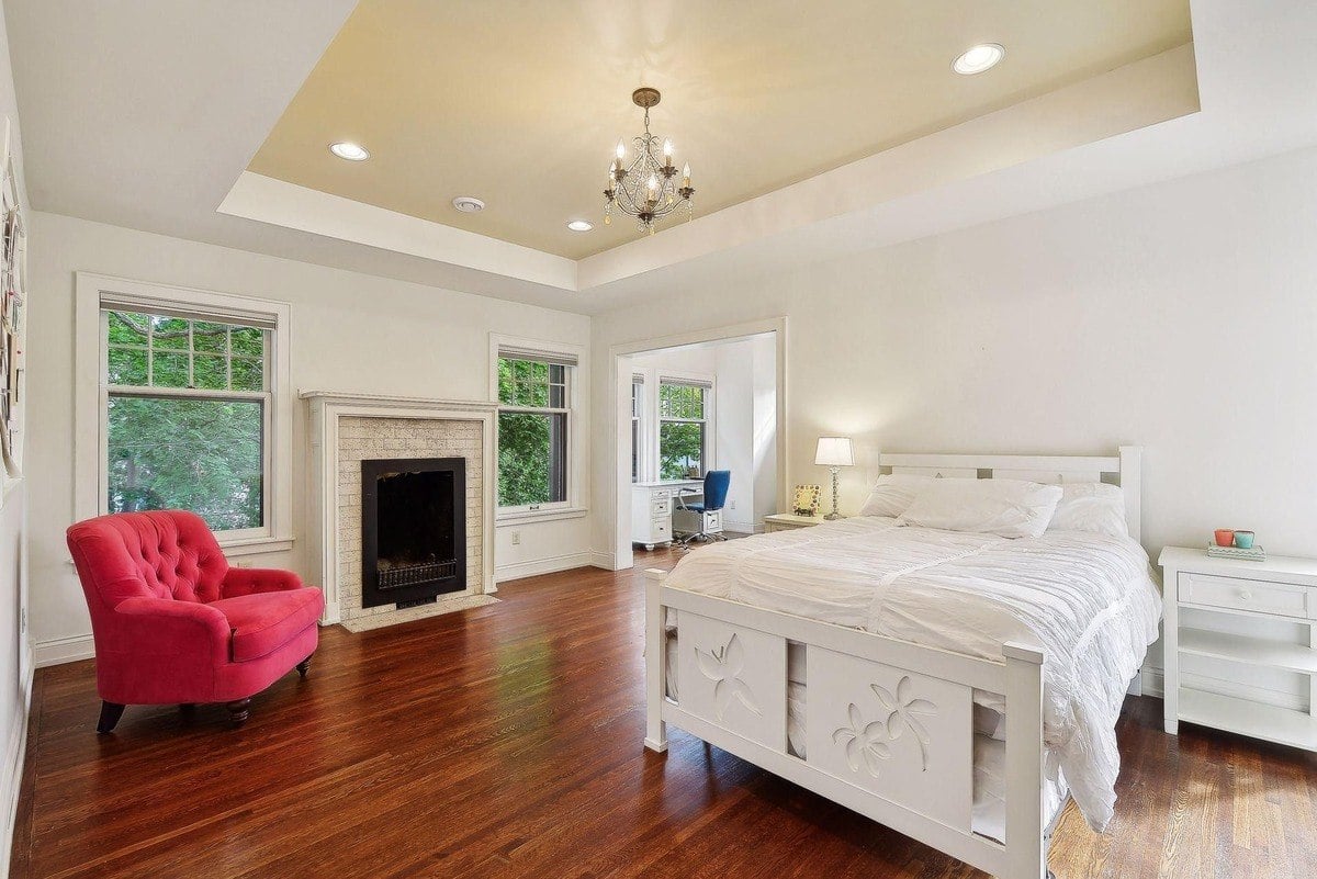 Bedroom with hardwood floors, a white bed, and a pink armchair.