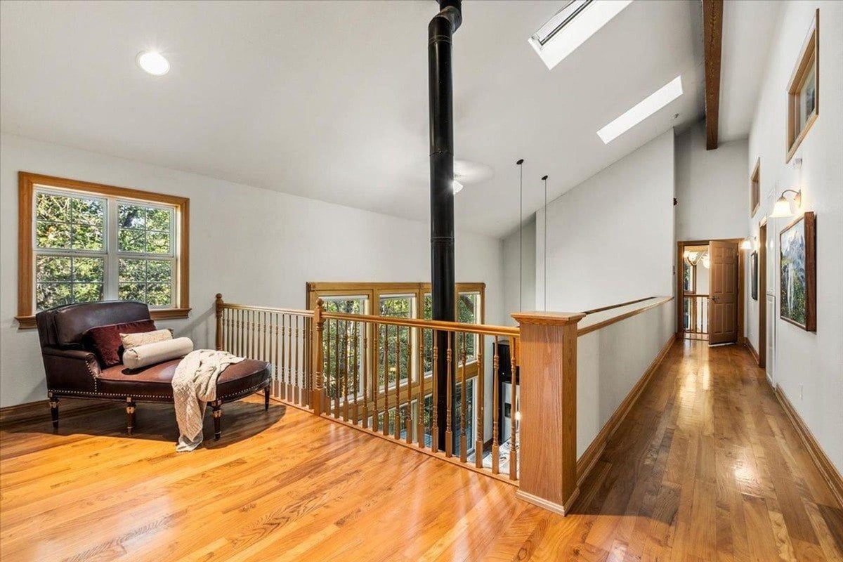 Open upstairs loft includes wood floors, a cozy chair, and a central stove pipe extending to the ceiling.