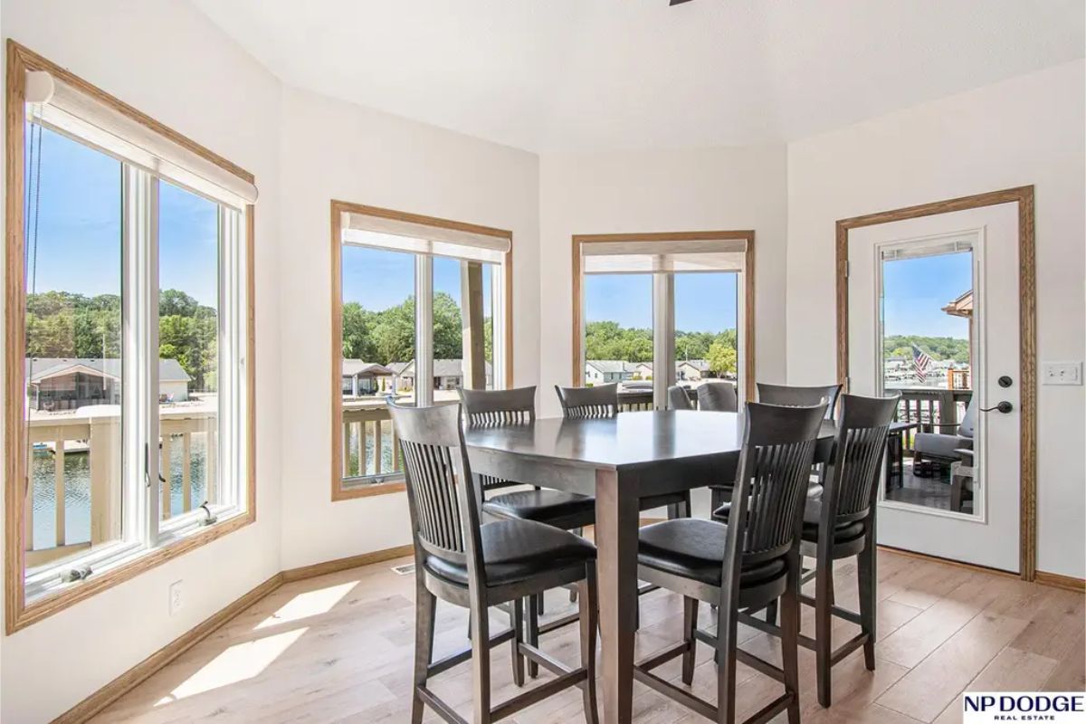 The dining room is surrounded by large windows offering panoramic views of the lake and abundant natural light.