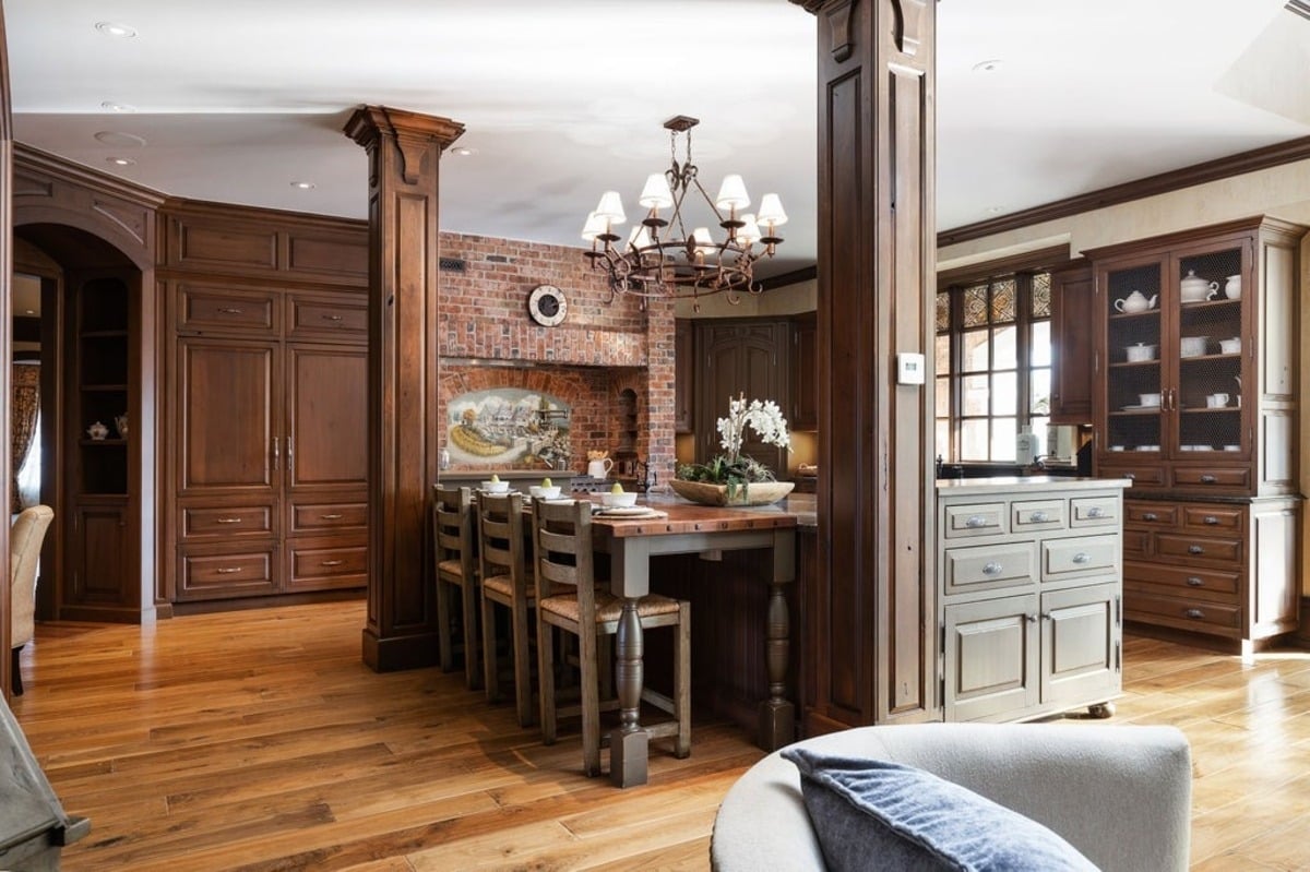 Cozy kitchen features warm wood cabinetry, a brick backsplash, and a large dining island with rustic decor.