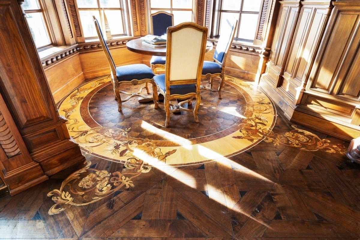 Dining nook is adorned with elaborate wood inlay flooring and classic upholstered chairs around a round table.