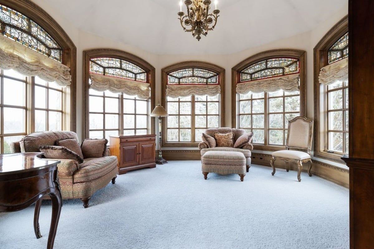 Sunlit lounge area is surrounded by arched windows with stained glass and soft, plush seating.