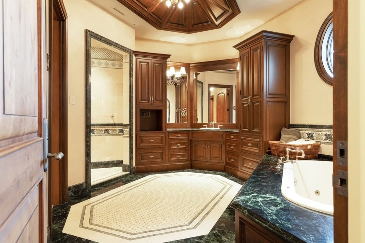 Luxurious bathroom combines dark wood cabinetry, green marble countertops, and a geometric floor design.