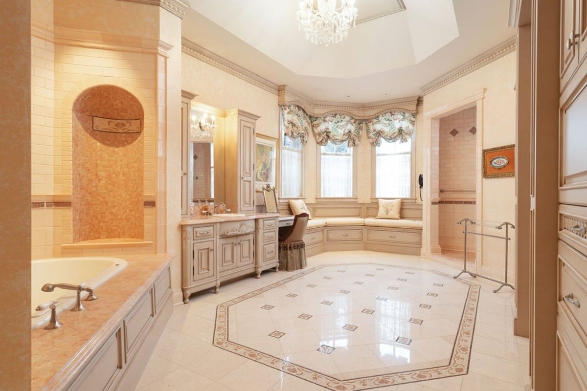 Elegant bathroom features light cabinetry, a large soaking tub, and a tiled seating alcove.