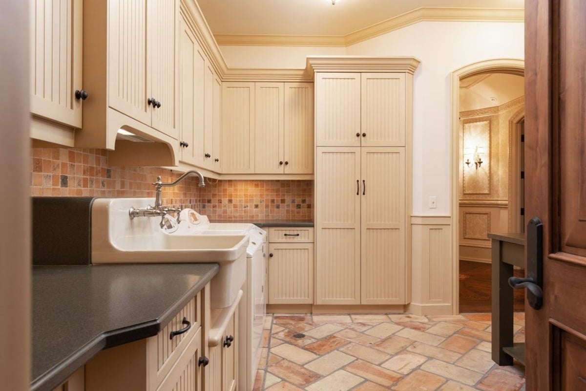 Functional utility room is designed with tiled floors, ample cabinetry, and a farmhouse sink.