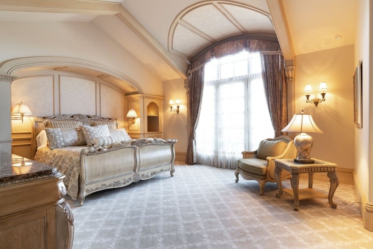 Refined bedroom pairs classic furniture with patterned wallpaper and a canopy-style bed.
