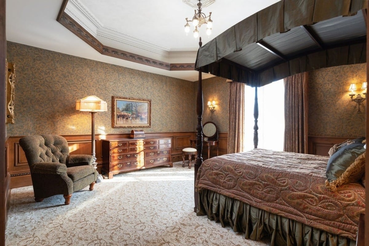 Luxurious bedroom features a canopy bed, classic wallpaper, and warm lighting, creating a cozy yet sophisticated atmosphere.