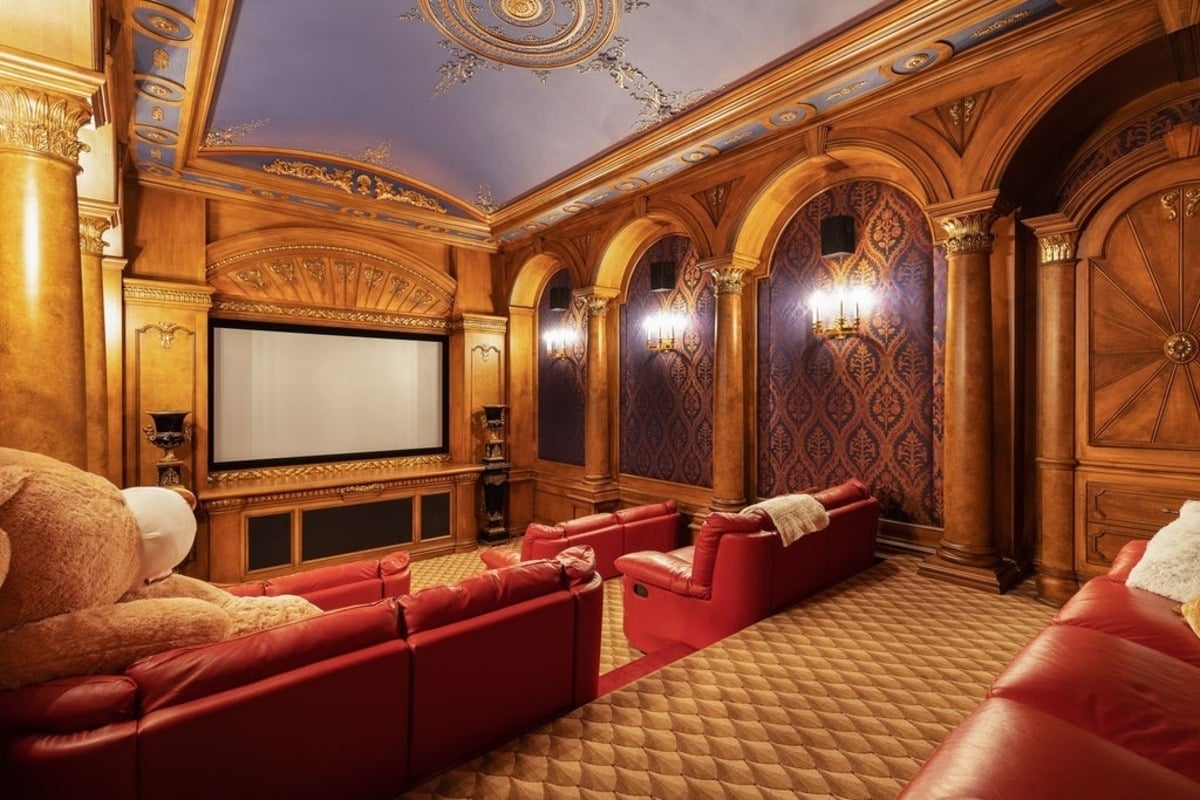 Home theater boasts ornate detailing, red leather recliners, and a regal color palette, perfect for an immersive movie experience.