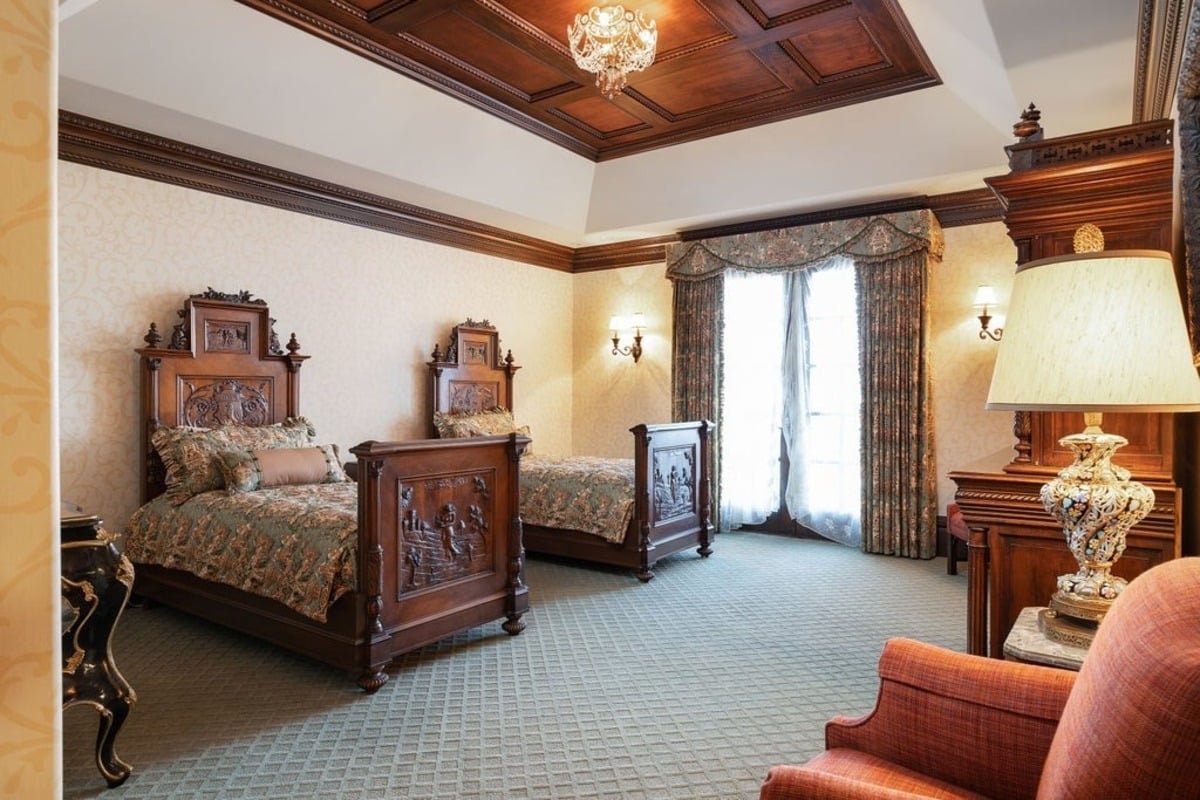 Bedroom showcases antique-style twin beds with carved wooden frames and a richly detailed coffered ceiling.