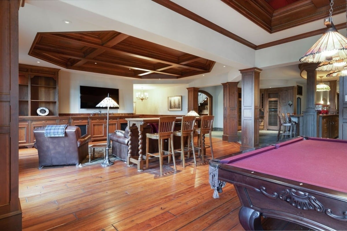 Entertainment room combines a pool table, bar area, and casual seating in a space accented by intricate woodwork.