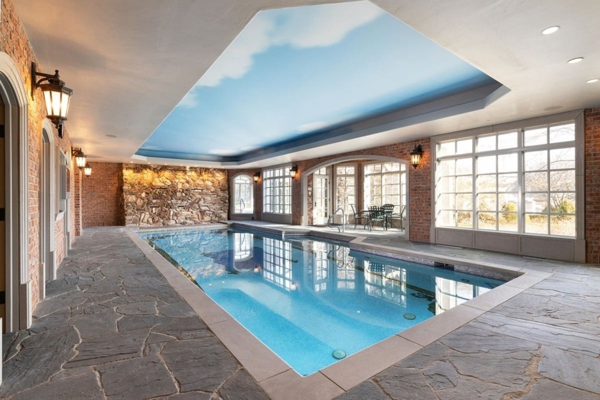 Indoor pool area features stone flooring, large windows, and a ceiling painted to resemble a clear sky.