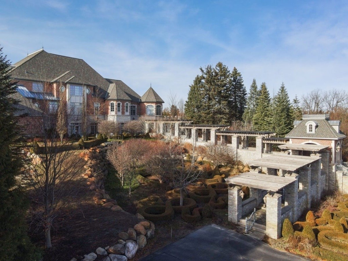 Landscaped backyard combines manicured hedges, stone pathways, and a pergola leading to a scenic retreat.