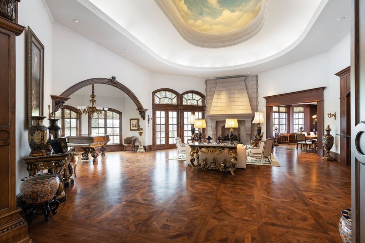 Living room with parquet flooring, a large fireplace, and a ceiling painted with a serene sky mural.