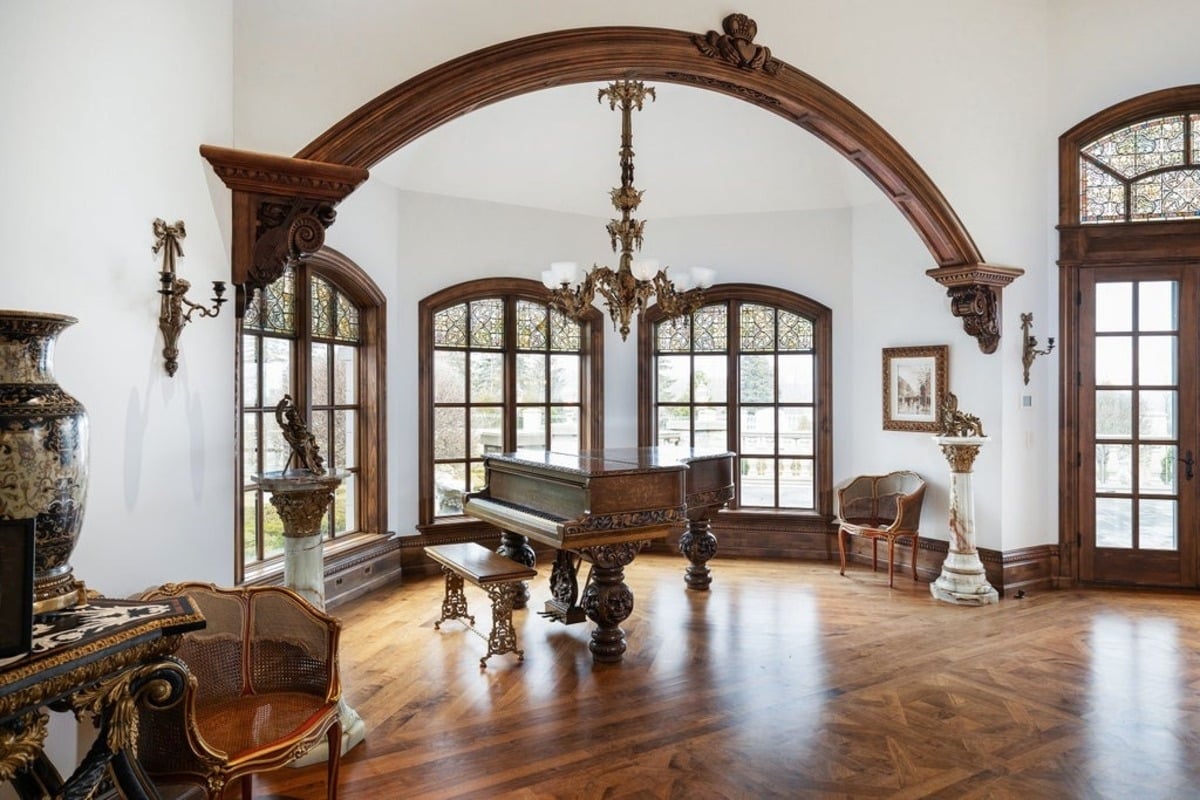 Music room framed by arched windows and highlighted by a vintage grand piano with detailed wood carvings.