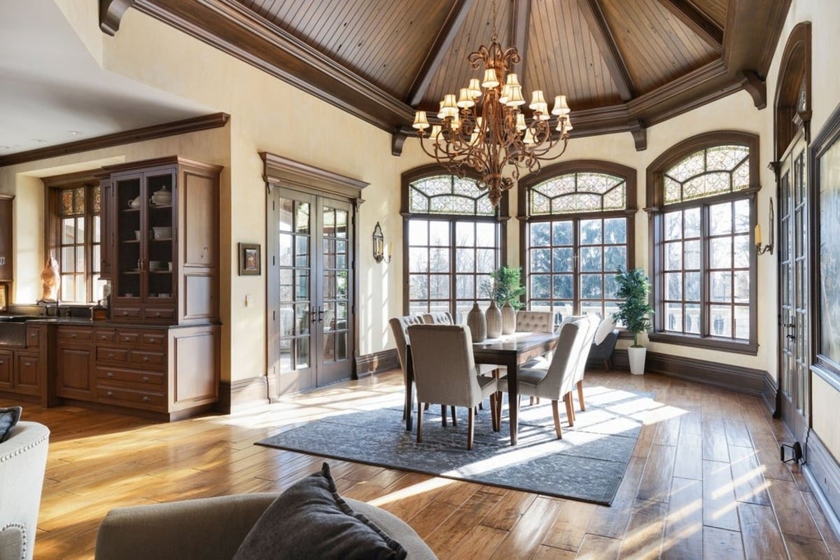 Dining nook illuminated by a central chandelier, surrounded by tall windows and wood paneling.