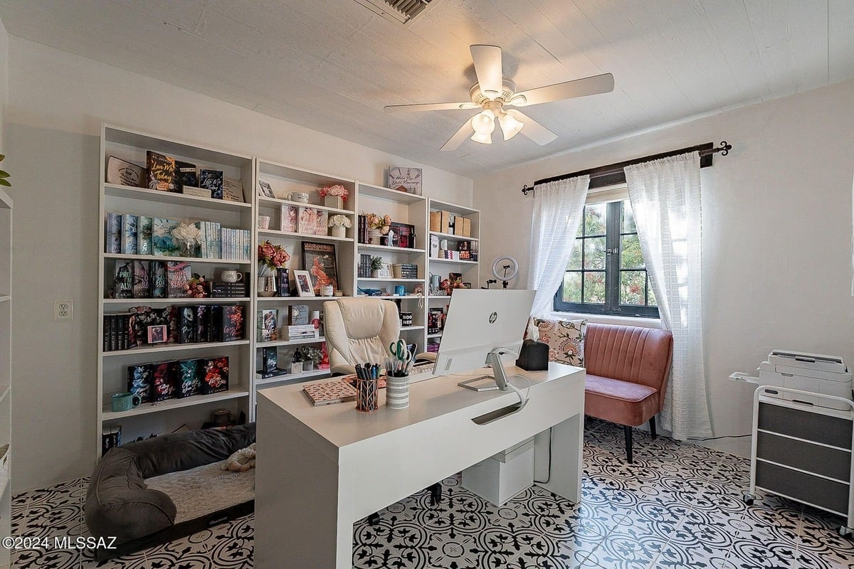 Home office with built-in bookshelves, a white desk, a pink chair, and a patterned floor.