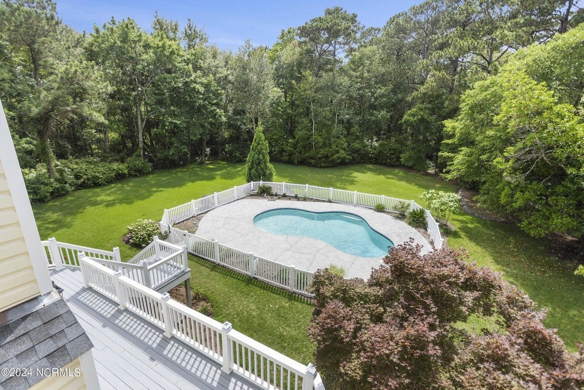 Backyard has kidney-shaped pool, green lawn, and trees.