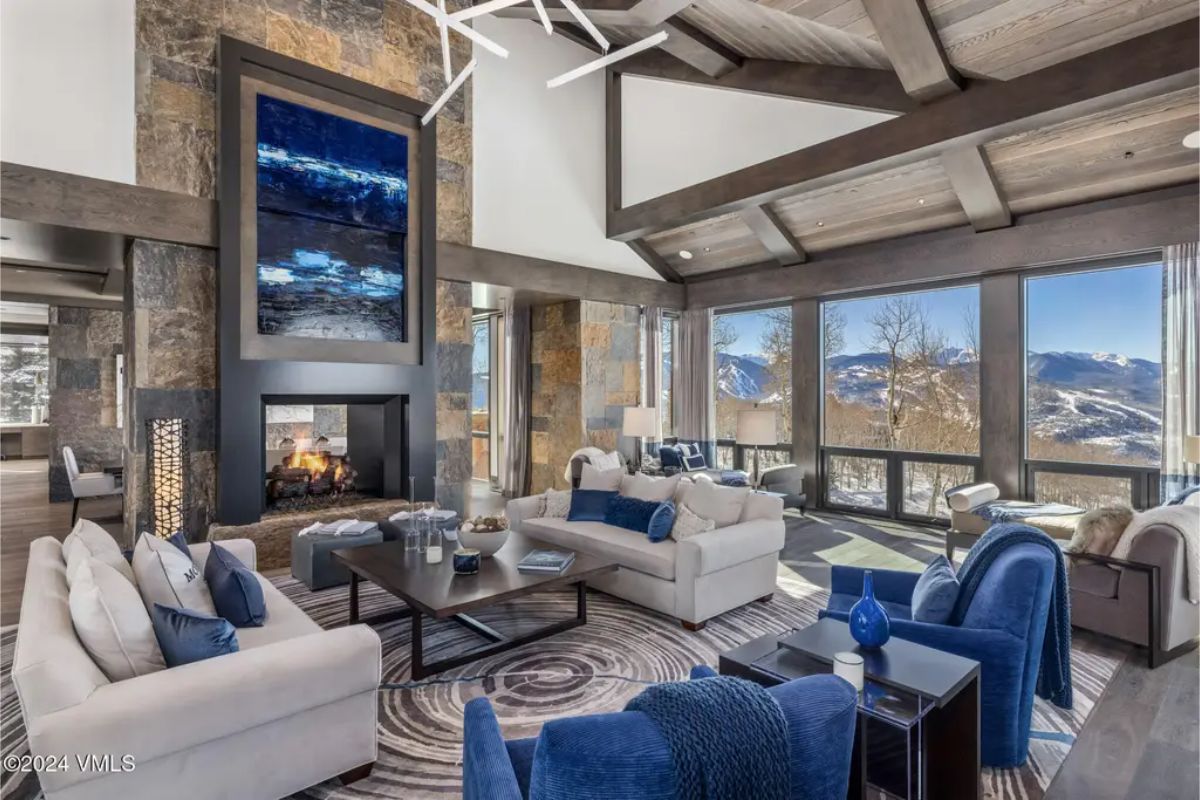 The living room features a vaulted ceiling with exposed beams and floor-to-ceiling windows, showcasing panoramic mountain views.