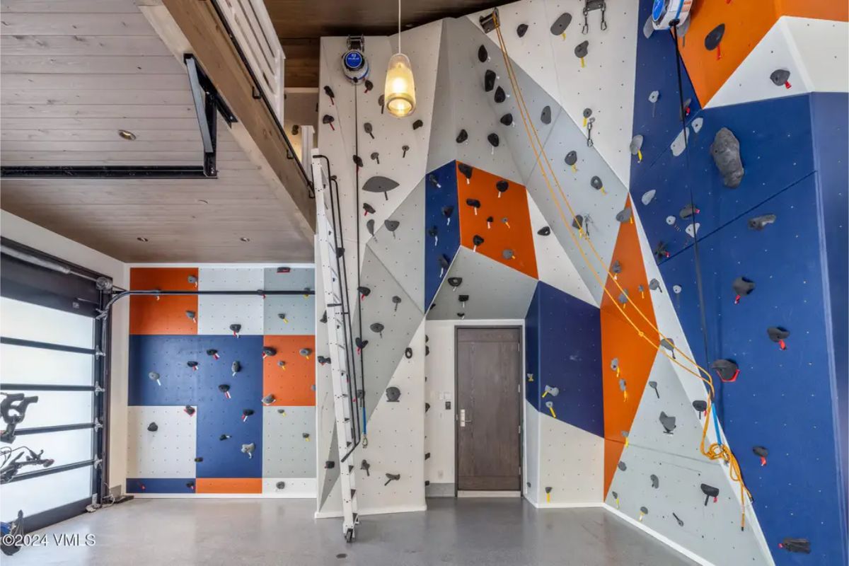 Custom-built indoor climbing wall features bold, geometric panels in blue, orange, and white.